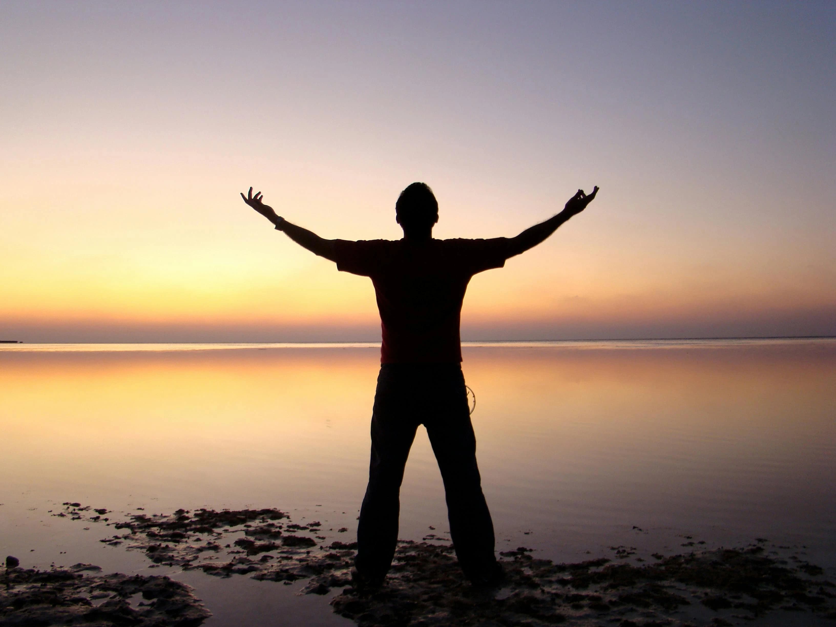 A man standing on a beach pointing hands to the sky
